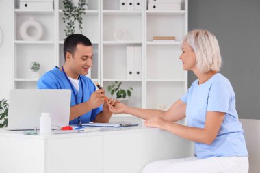 Kan şekerini ölçen tükenmez kalemli erkek endokrinolojist klinikteki masada olgun bir kadın var.