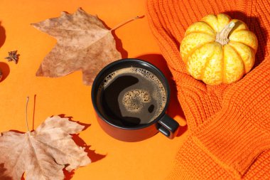 Bir fincan lezzetli balkabağı kahvesi, sonbahar süslemeleri ve turuncu arka planda sıcak süveter.