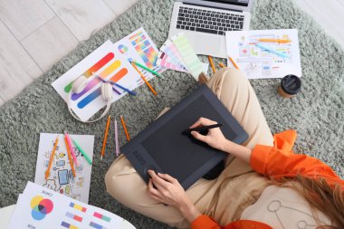 Ofisteki halı üzerinde grafik tabletle çalışan kadın web tasarımcısı, üst görünüm