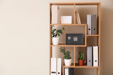 Modern kasa, ofis dosyaları ve bej duvarın yanındaki raf ünitesinde bulunan ev bitkileri.