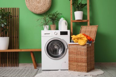 Çamaşır odasının içinde hasır çamaşır sepeti, çamaşır makinesi ve ev bitkileri var.