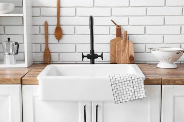 Beyaz seramik lavabo ve raf ünitesi mutfaktaki beyaz tuğla duvarın yanındaki ahşap tezgahta.