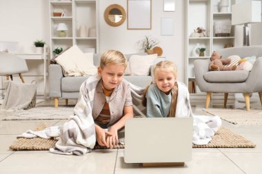 Evde dizüstü bilgisayar kullanan ekose elbiseli küçük bir kız ve oğlan.