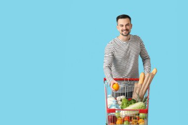 Mavi arka planda alışveriş arabası olan mutlu genç bir adam.
