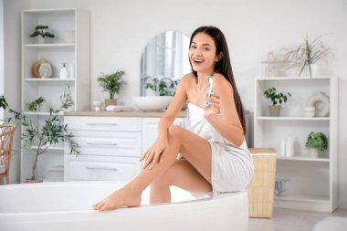 Güzel, genç ve mutlu bir kadın banyoda jiletle oturuyor.