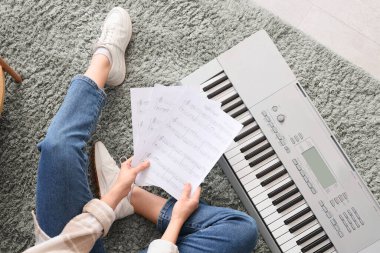 Çarşafları ve sentezleyicisi olan genç bir kadın halıda oturuyor.