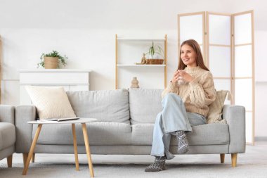 Evdeki kanepede çay içen genç bir kadın.