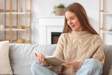 Evdeki kanepede kitap okuyan genç bir kadın.