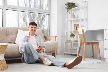 Evdeki kanepenin yanında cep telefonu kullanan genç bir adam.