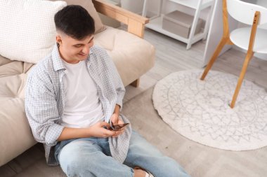 Evdeki kanepenin yanında cep telefonu kullanan genç bir adam.