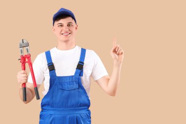 Cıvata keskisi olan erkek işçi bej arka plandaki bir şeyi işaret ediyor.