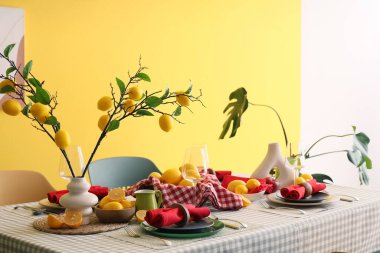 Yemek odasındaki sarı duvarın yanında taze narenciye ve güzel limon dallarıyla süslenmiş şık bir masa.