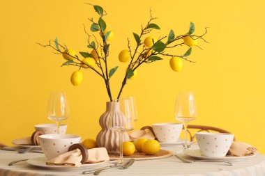 Yemek odasındaki sarı duvarın yanında güzel limon dallarıyla süslenmiş şık bir masa.