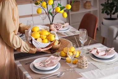 Yemek odasında bir kase taze limonla masa dekorasyonu yapan genç bir kadın.