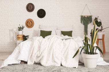 Sandalye, şapka ve yeşil bitkilerle aydınlık yatak odasının içinde.