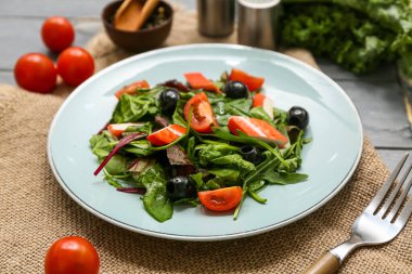 Yengeç çubuklu bir tabak salata, ıspanak, siyah zeytin ve peçeteli domates.