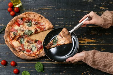 Siyah ahşap kaplama tabakta lezzetli bir pizza ile kadın elleri. Üst görünüm