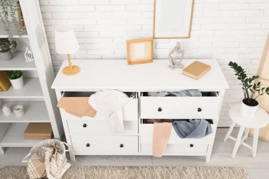 Oturma odasındaki beyaz tuğla duvarın yanında dağınık giysilerle tuvalet.