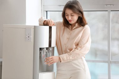 Güzel genç bir kadın mutfaktaki soğutucudan cama su dolduruyor.