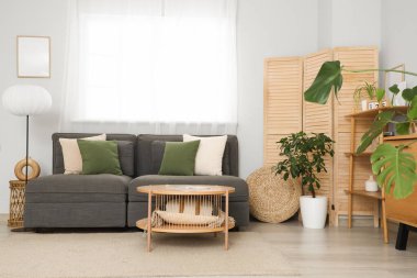 Oturma odasının içinde siyah kanepe, lamba ve katlanır ekran var.