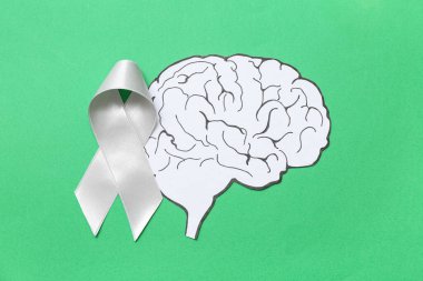 Yeşil arka planda gri farkındalık kurdelesi olan kağıt beyin. Kanser kavramı
