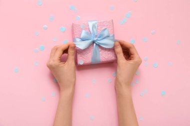 Hediye kutusu ve pembe arka planda mavi konfeti olan kadın elleri.