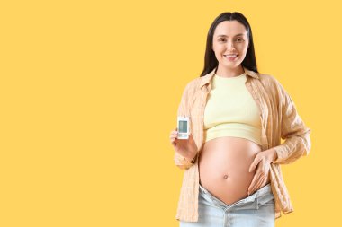 Sarı arka planda glukometresi olan hamile bir kadın. Gebelik Diyabet Konsepti