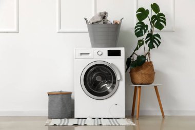 Banyoda beyaz duvarın yanında çamaşır sepeti olan modern çamaşır makinesi.