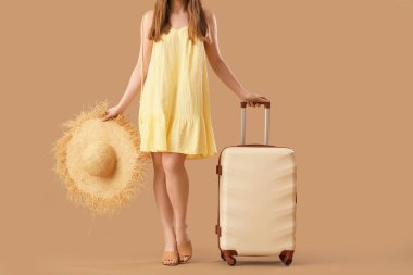 Bavulu ve bej arka planda hasır şapkalı genç bayan, yakın plan. Seyahat kavramı