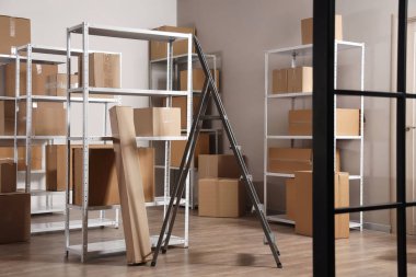 Deponun içinde raf üniteleri, karton kutular ve merdiven var.