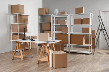 Deponun içinde raf üniteleri, karton kutular ve işyeri var.