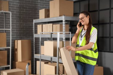 Depoda cep telefonuyla konuşan paketli bir kadın işçi.