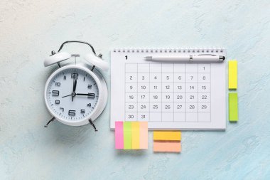 Alarm saati, kalem ve renk arkaplanı üzerine yapışkan notlar içeren bir takvim. Planlama kavramı