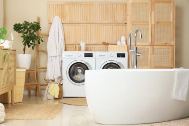 Modern çamaşır makineleri, banyo küveti ve banyo aksesuarları olan şık bir çamaşırhane.