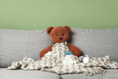 Termometresi olan oyuncak ayı, yeşil duvarın yanındaki koltukta haplar ve mendiller. Soğuk kavram