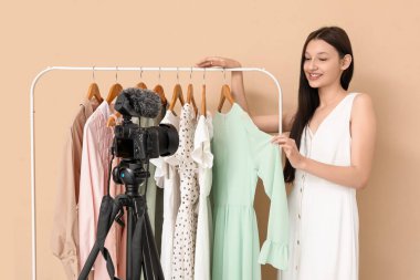 Bej arkaplan üzerine elbise askılığı kayıt videosu olan genç blog yazarı