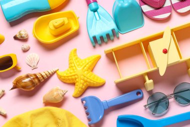 Pembe arka plandaki çocuklar için kumsal kalıpları, deniz kabukları ve plaj aksesuarları olan kompozisyon, yakın plan