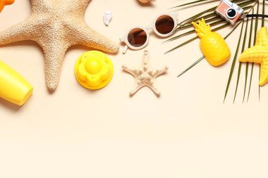 Deniz yıldızları, güneş kremi, güneş gözlüğü ve bej arkaplanda kumsal kalıpları olan kompozisyon