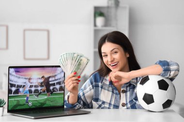 Evdeki spor bahsini kazandıktan sonra parası ve futbol topu olan mutlu genç bir kadın.