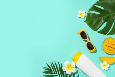 Mangolu yaz kompozisyonu, bir şişe güneş kremi ve turkuaz arka planda tropikal yapraklar.