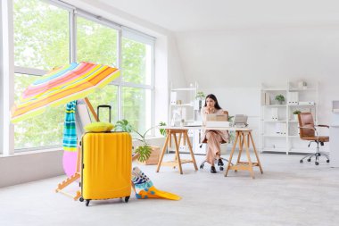 Valiziyle ofiste tatil bekleyen üzgün bir iş kadını.