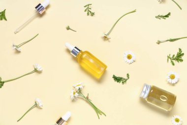 Sarı arka planda papatya çiçeği ve kozmetik yağı şişeleri