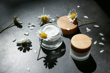 İçinde doğal krema kavanozları ve koyu arkaplanda papatya çiçekleri olan kompozisyon