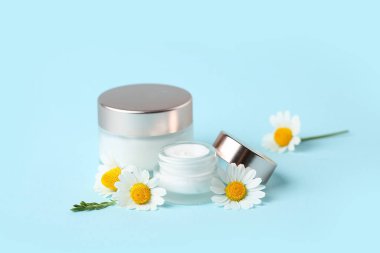 Doğal krema kavanozları ve renk arkaplan üzerinde papatya çiçekleri olan kompozisyon