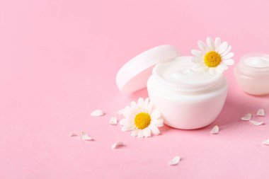 İçinde doğal krema kavanozları ve pembe arka planda papatya çiçekleri olan kompozisyon