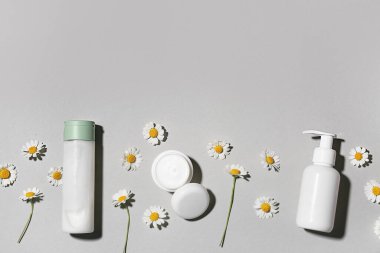 Gri arka planda farklı papatya çayı kozmetik ürünleri ve çiçekler