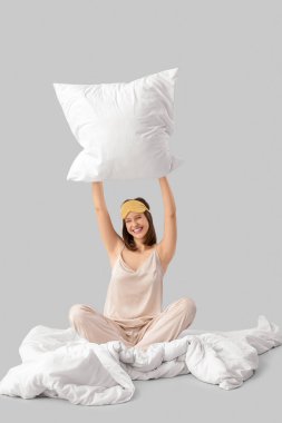 Yastıklı pijamalı genç bir kadın açık arka planda battaniyede oturuyor.