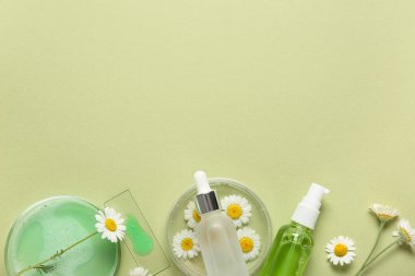 Yeşil arka planda papatya çiçekleri, test kaseleri ve kozmetik ürünleri şişeleri olan kompozisyon, yakın plan