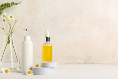 Papatya çiçekleri, alçı podyumlar ve bej duvarın yanındaki masada bulunan kozmetik ürünler.