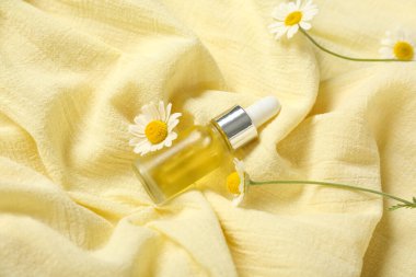 Arka plan olarak sarı kumaş üzerine papatya çiçekleri ve bir şişe kozmetik ürünü içeren kompozisyon, yakın plan.